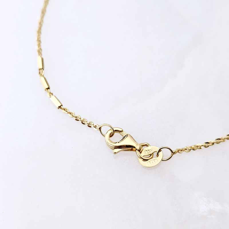 A close-up of a gold chain necklace with a lobster clasp and a small heart-shaped charm engraved with 'LOVE' and '10M', displayed on a light gray background.