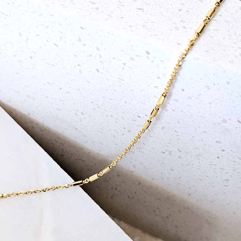 A close-up of a delicate gold chain necklace draped diagonally across a textured white surface.