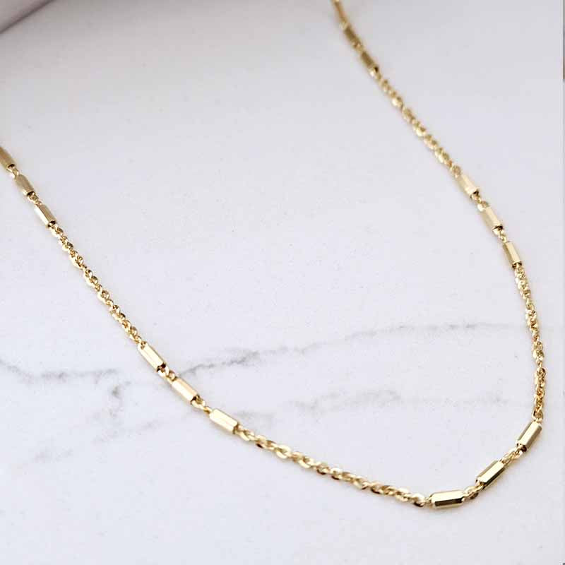 A gold chain necklace with rectangular link accents, displayed on a light gray marble surface.