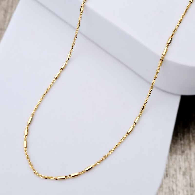 A gold chain necklace with elongated rectangular links, draped elegantly over a white display stand.