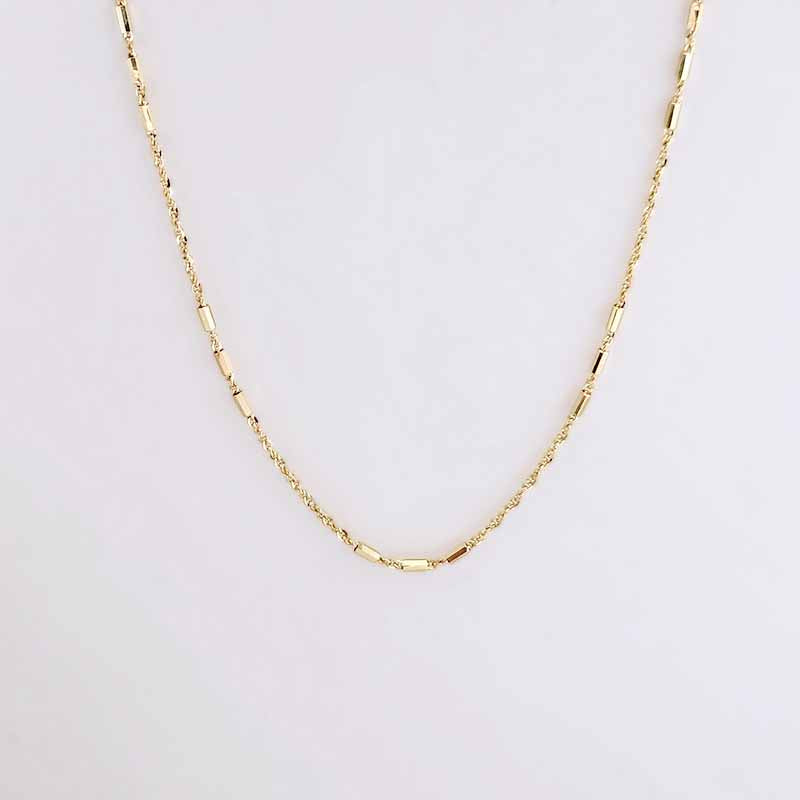 A delicate gold chain necklace with a unique textured link design, displayed against a clean, light off-white background.