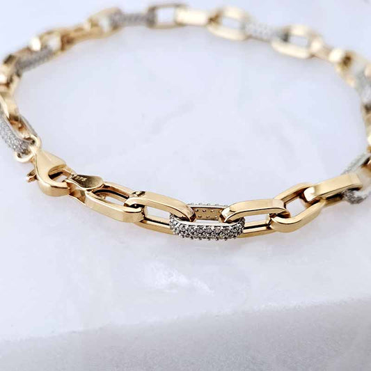 A close-up of a gold and white-gold chain bracelet with a central pavé-set accent, displayed on a white marble surface.
