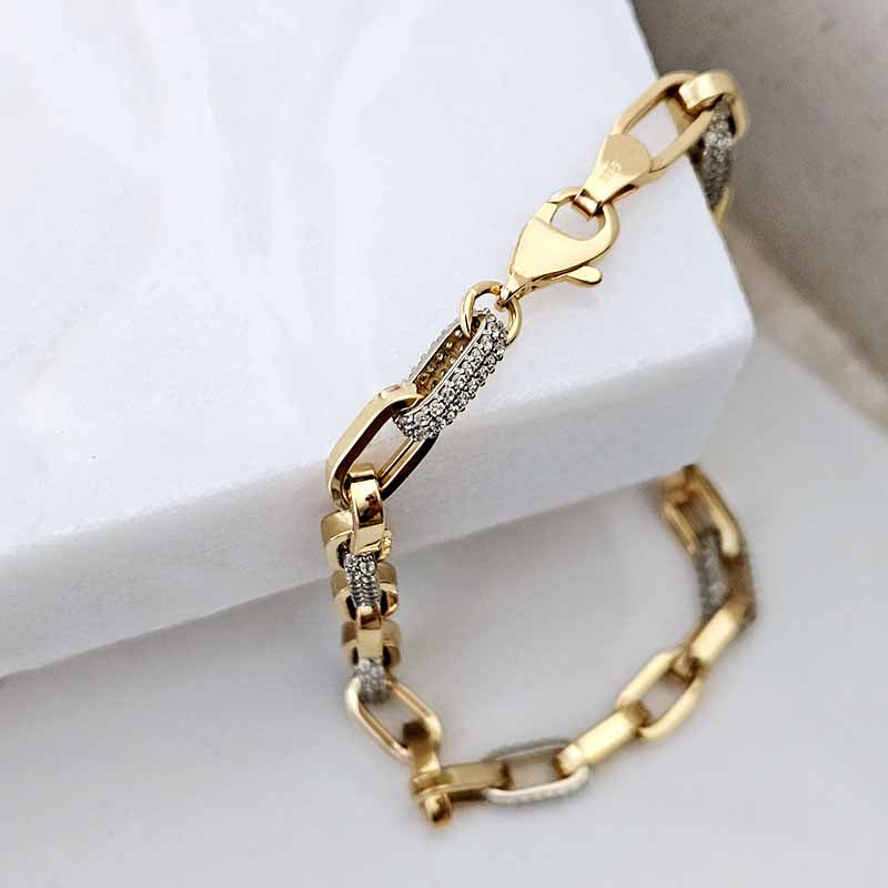 A gold chain link bracelet with pavé crystal accents, displayed on a white jewelry stand.