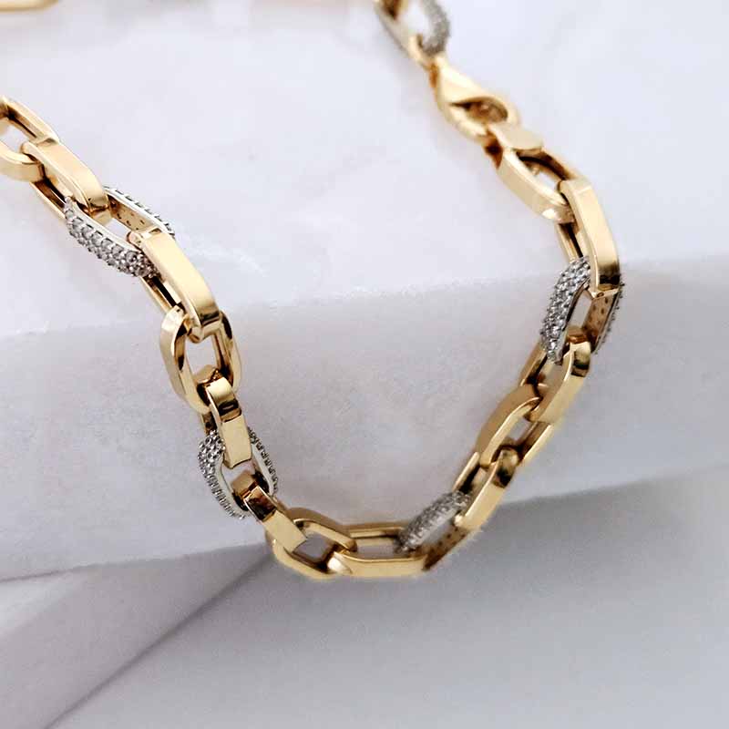 A close-up of a gold chain necklace with textured silver pavé links, resting on a white textured surface.